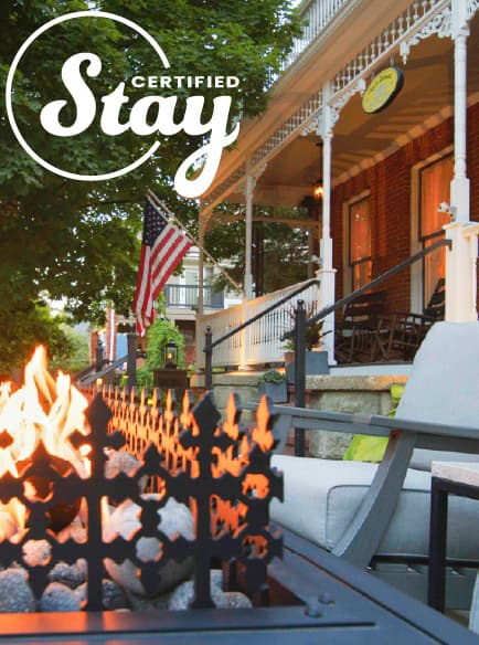 A cozy porch with a fire pit, surrounded by greenery and featuring an American flag.