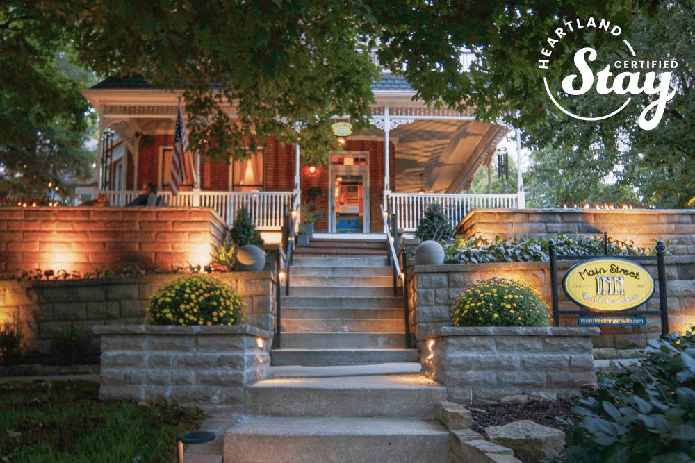 Historic house with illuminated steps leading to a welcoming porch, framed by lush greenery and flowers.