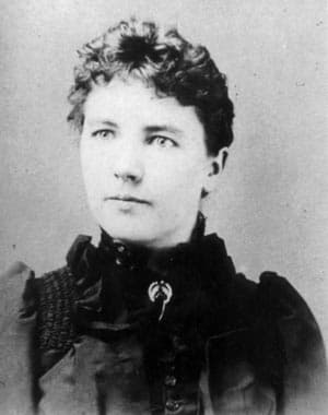 A black-and-white portrait of a woman with short, curly hair, wearing a Victorian-style dress.